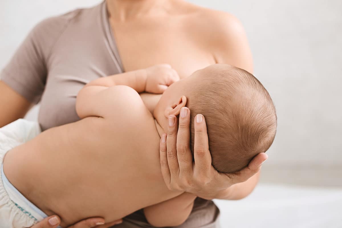 Mother breastfeeding and hugging her newborn baby