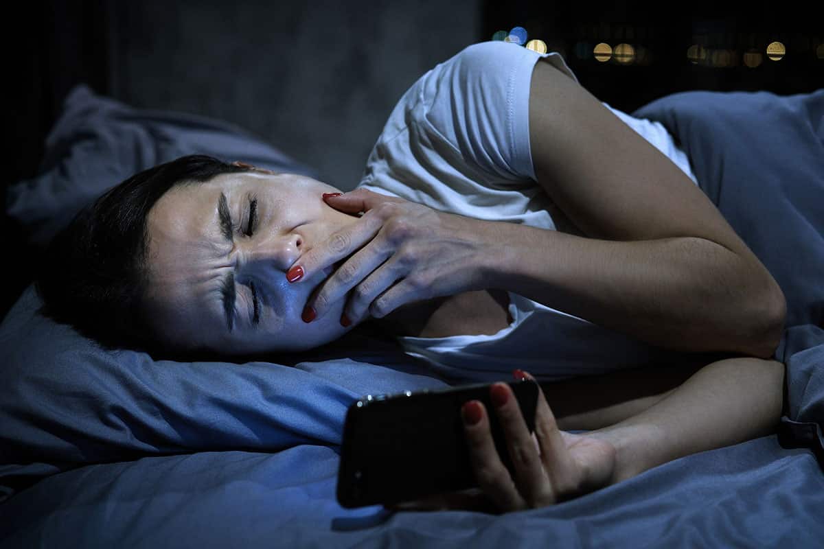 Young sleepy female using mobile phone